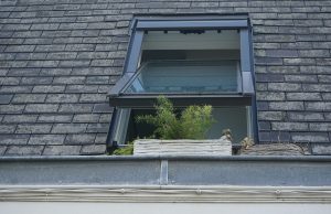 Open window with potted plants on the ledge against a slate roof.